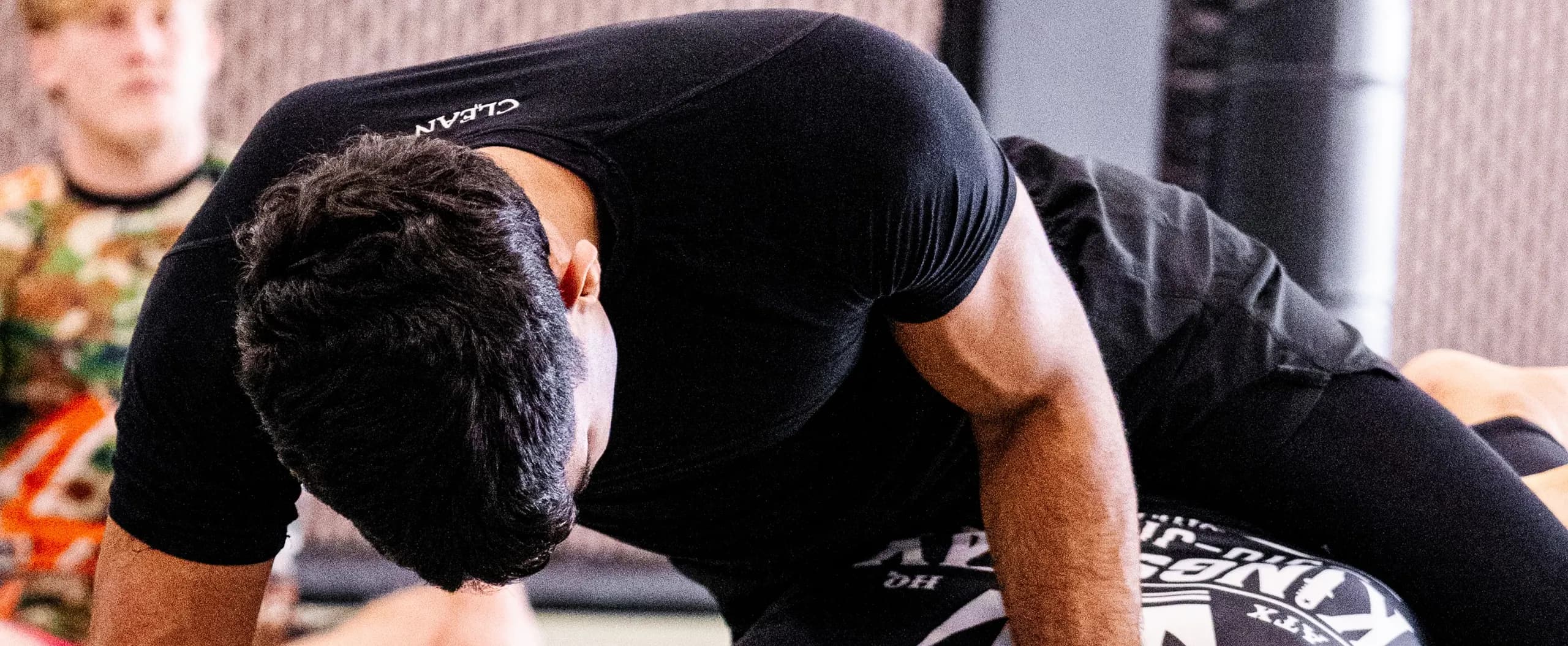 Leaning over a training partner in the black short-sleeve rash guard, with the CLEAN wordmark across the upper back.
