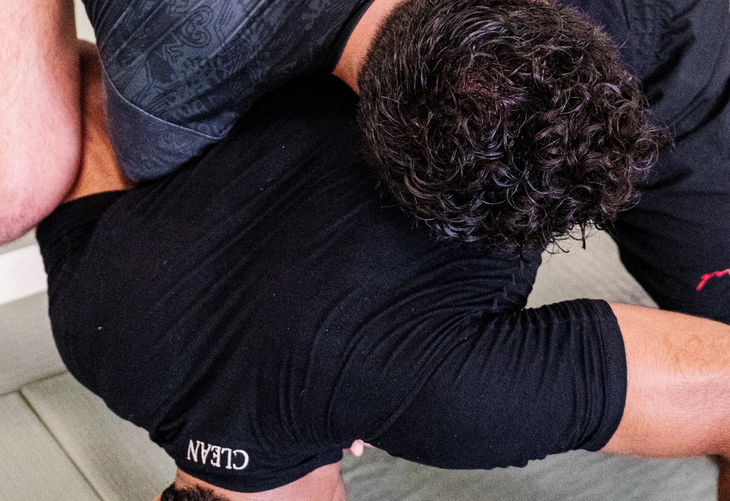 The short-sleeve rash guard stretched across the back during a roll, with the CLEAN wordmark at the hem.